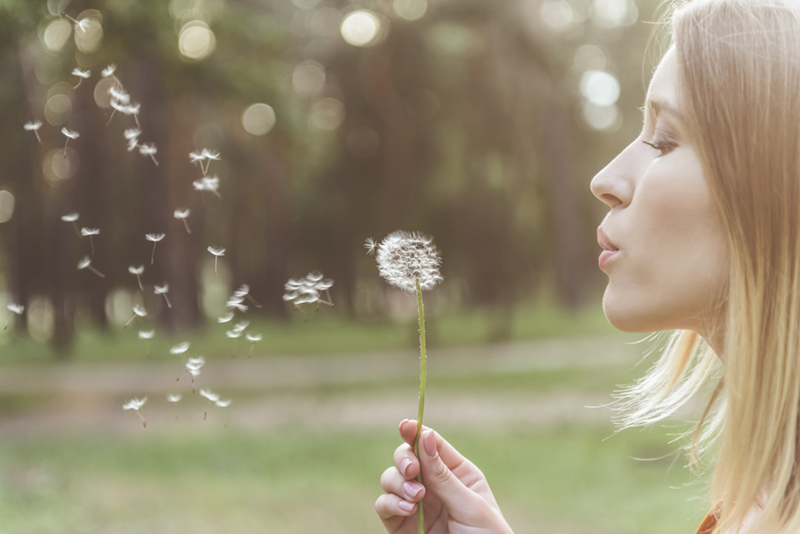 woman blowing a dandelion outside